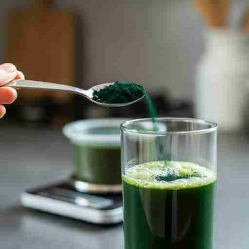 Come usare la spirulina per dimagrire Cucchiaino che versa polvere di spirulina in un frullato verde, accanto a una bilancia da cucina di precisione