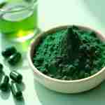 Spirulina per la pelle: Segreto Naturale di Giovinezza: Un'immagine vibrante e ravvicinata di polvere o capsule di spirulina posizionate accanto a una piccola ciotola di acqua o prodotti per la cura della pelle. Lo sfondo dovrebbe essere minimale e pulito, evidenziando il ricco colore verde della polvere di spirulina. L'immagine dovrebbe trasmettere un senso di benessere naturale e benefici per la cura della pelle.