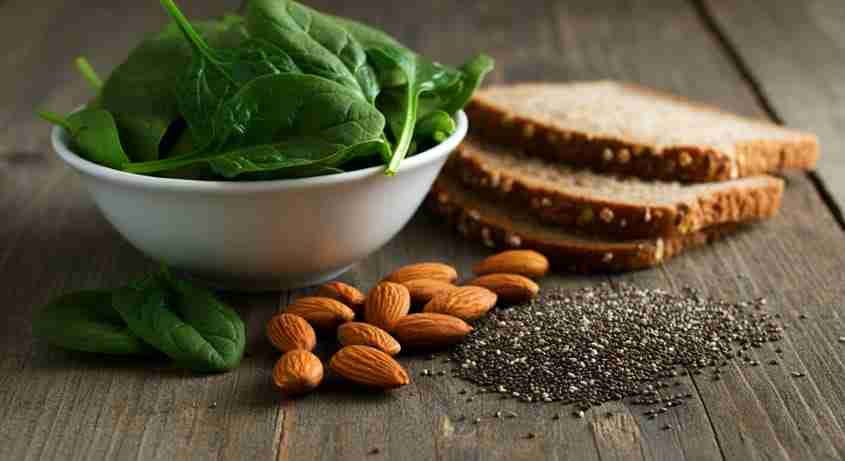 L'Importanza Fondamentale del Magnesio nel Corpo Umano: Variety of magnesium-rich foods arranged on a wooden table, including dark leafy greens, nuts, seeds, and whole grains